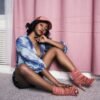 Elegant woman in stylish outfit poses by pink curtain indoors, showcasing modern fashion and beauty.