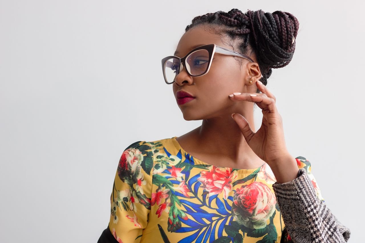 Elegant portrait featuring a woman in glasses with braided hairstyle and floral top.